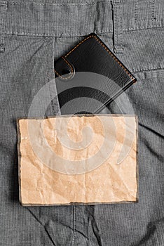 Small wallet in the trousers front pocket beside brown note sheet. Little purse is placed inside man pants near notation