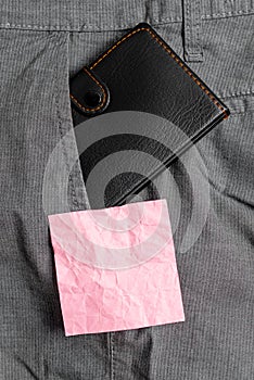 Small wallet in the trousers front pocket beside pink note sheet. Little purse is placed inside man pants near notation