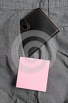 Small wallet in the trousers front pocket beside pink note sheet. Little purse is placed inside man pants near notation