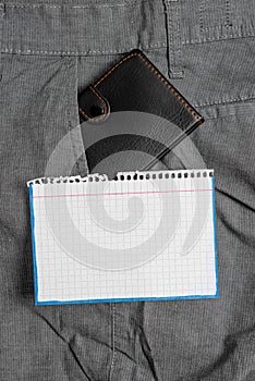 Small wallet in the trousers front pocket beside white note sheet. Little purse is placed inside man pants near notation