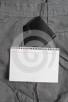 Small wallet in the trousers front pocket beside white note sheet. Little purse is placed inside man pants near notation