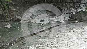 Small water stream flowing in the channel. Concrete pipe and wall. Dry irrigation canal and water drainage system.