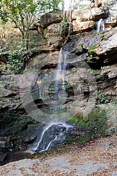 Small waterfall, with crystal clear water, many rocks and large trees around in the middle of the forest.