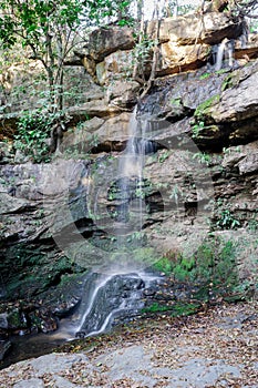Small waterfall, with crystal clear water, many rocks and large trees around in the middle of the forest.