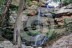 Small waterfall, with crystal clear water, many rocks and large trees around in the middle of the forest.