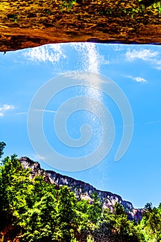 A waterfall flowing over the cliffs overhanging the trail to the Lower Emerald Pool in Zion National Park, Utah, United States