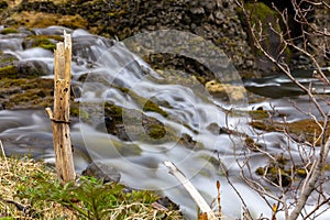 Small waterfall with flowing water over the stones surrounded by green vegetation in Gjain Canyon in Thjorsardalur valley, Iceland