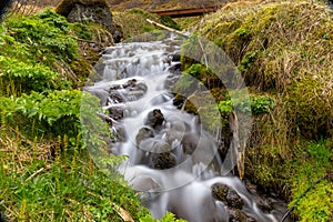 Small waterfall with flowing water over the stones surrounded by green vegetation in Gjain Canyon in Thjorsardalur valley, Iceland