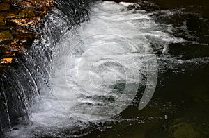 A small waterfall. The height difference of the water flow in the river is equipped with round wooden log