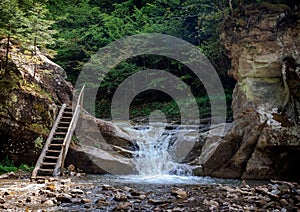 Small waterfall and ladder between rocks in a mountain forest