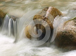 Small waterfall in the mountain river. Beautiful natural background of stones and with flowing, blurring water and foaming.