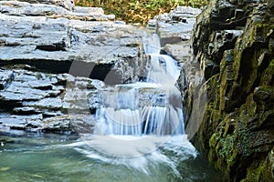 Small waterfall in a mountain stream between rocks, the water is blurred in motion