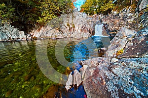 Small waterfall over rocks into blue and green river next to huge boulders in forest
