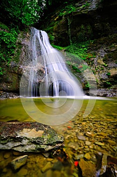 a small waterfall running between two rocks in a stream near trees