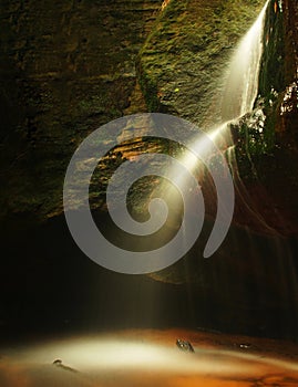 Small waterfall on small mountain stream, mossy sandstone block and water is jumping down into small pool. Water streams with