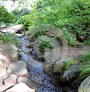 Small waterfall on the stones, grass, bushes in the summer   park,  in Kotka, Finland