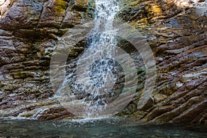 Small waterfall on a textured stone wall on the river Krikiliotis at Panta Vrexei in Evritania, Greece