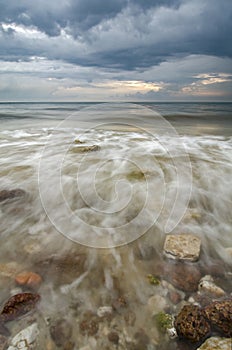 While small wave hitting stone at the beach with dramatic dark clouds background before storm