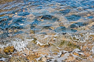 A small wave rolls on the seashore. Multi-colored stones underwater. Background
