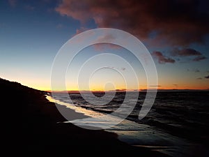 Small wave on the surface of the sea and a dark sandy beach against the blue sky after sunset