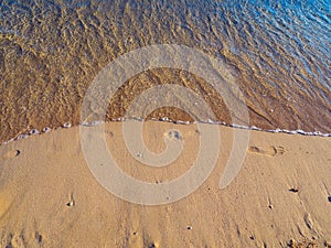 Small wave washing away footprints in the sand - on the beach