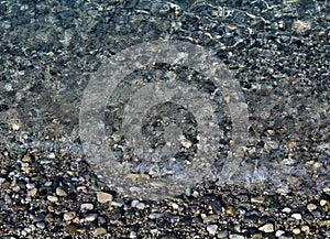 Small wavelets breaking on the seashore covered by pebbles and cobbles