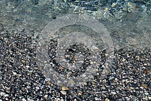 Small wavelets breaking on the seashore covered by pebbles and cobbles