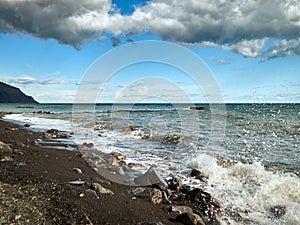 small waves roll on the rocky shore, splashes of water, blue sky with clouds