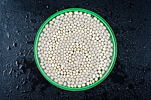 Small white beans of the Nevi variety on a round green plate on a black wet background