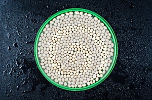 Small white beans of the Nevi variety on a round green plate on a black wet background photo