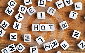 Small white and black bead cubes on wooden board, letters in middle spell HOT.