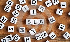 Small white and black bead cubes on wooden board, letters in middle spell SLA - Service Level Agreement concept.