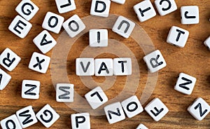 Small white and black bead cubes on wooden board, letters in middle spell VAT - Value Added Tax