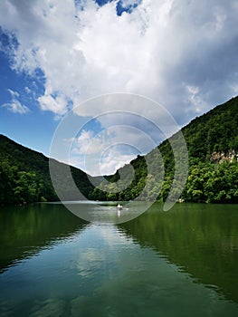 Small white boat on a calm lake with green mountains in the background on a cloudy day