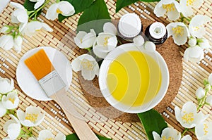Small white bowl with cosmetic aroma oil, small bottles with essential oil, make-up brush and white jasmine flowers. Natural spa