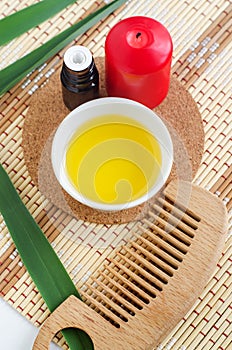 Small white bowl with cosmetic cleansingoil, small bottle with essential oil, red candle and wooden hair brush. Natural spa