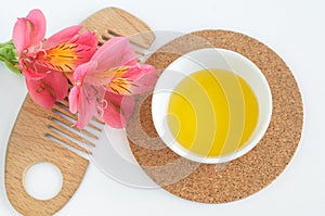 Small white bowl with cosmetic oil, red flowers and wooden hair brush. Natural spa and beauty treatment recipe. Top view