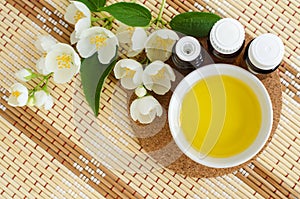 Small white bowl with cosmetic oil, small bottles with essential oil and white jasmine flowers. Natural spa and beauty treatment