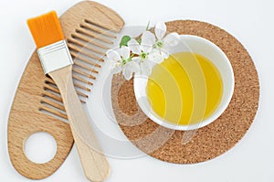 Small white bowl with cosmetic oil, white flowers, make-up brush and wooden hair brush. Natural spa and beauty treatment recipe.