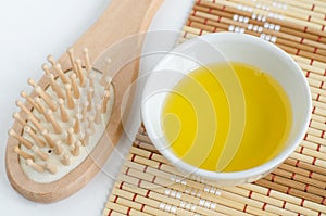 Small white bowl with cosmetic oil and wooden hair brush. Natural spa, hair care and beauty treatment recipe.