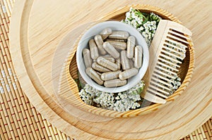 Small white bowl with food supplement capsules, wooden hair brush and yarrow flowers. Natural healthcare, herbal medicine