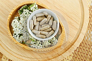 Small white bowl with food supplement capsules and yarrow flowers. Natural healthcare, herbal medicine, skincare and beauty
