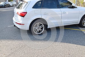 Small white car with a flat rear tire on an asphalt road