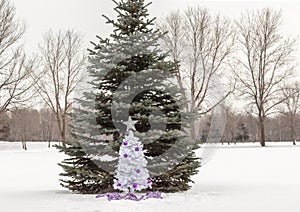 Small white christmas tree with purple and silver decorations standing in snow