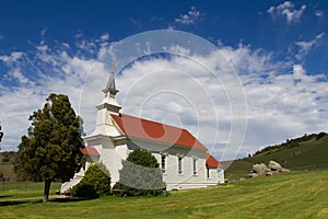 Side angle of a little white church with a red roof in Northern California with patchy blue skies photo