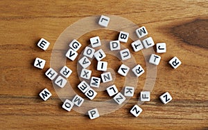 Small white cube beads with various letters scattered on wooden board, view from above