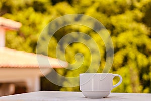 A small white cup of coffee on a blurry natural background