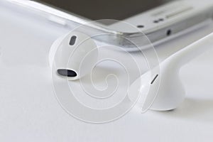 Small white ear buds lying next to a cell phone.