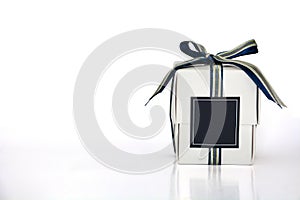 Small white gift box wrapped with blue, silver and golden color ribbon and dark blue blank label on white background, copy space
