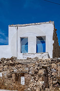 Small white house with blue color door and window, wooden frames on whitewashed  wall, greek island architecture, clear blue sky